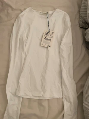 Vit långärmad topp från Pull&Bear - Klassisk vit långärmad topp från Pull&Bear i enkel och stilren design. Tillverkad i mjuk bomull med rund halsringning och normal passform. Perfekt basplagg att styla till olika outfits.