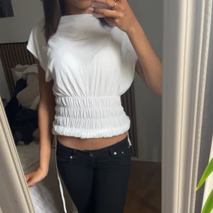 Vit topp med smock från Musera - Har andvänts 1 gång sen den köptes.  en vit topp från Musera med bred smock i midjan som ger en snygg siluett. Toppen har korta ärmar och är tillverkad i ett mjukt material som känns skönt mot huden. Perfekt att styla med jeans eller kjol för en fräsch look.