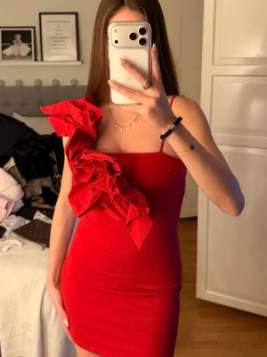 Röd one shoulder klänning med volang - Snygg röd kortklänning med one shoulder-design och stora volangdetaljer längs axeln och bröstet. .