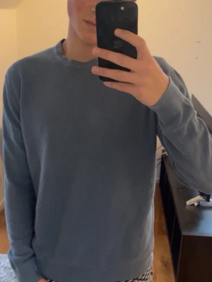 Blå stickad tröja från springfield  - Snygg blå stickad tröja från Springfield med rund halsringning och diskret struktur i materialet. Tröjan har långa ärmar och ribbade muddar vid ärmslut och nederkant. De är en Storlek M. Modellen i bilden är 188cm lång och väger 74kg 