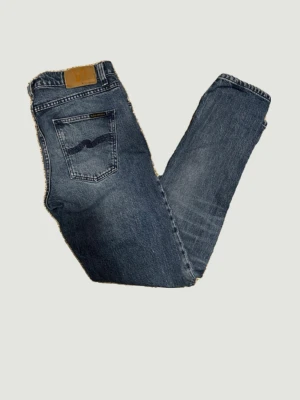Blå jeans från Nudie Jeans - Säljer ett par klassiska blå jeans från Nudie Jeans med snygg tvätt och raka ben. Jeansen har fem fickor, kontrastsömmar och Nudie-loggan på bakfickan. Tillverkade i slitstark denim med en skön passform. Storlek W29 L32.