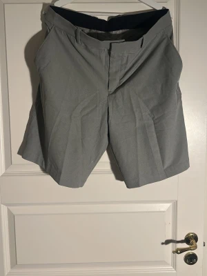Gråa klassiska shorts från Nike - Snygga grå shorts med normal passform och klassisk design. De har bälteshällor, framfickor och två bakfickor. Perfekta för sommaren och tillverkade i ett mjukt bomullsmaterial. Stängs med dragkedja och knapp framtill.