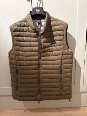 Brun dunväst från Colmar - Snygg brun dunväst från Colmar med quiltad design plugged med dragkedja framtill och två praktiska fick sop dragkedja. Märkeslogga på bröstet och ståkrage för extra tuff look. Perfekt för lager-på-lager och streetstyle. Nästan helt ny så inga skador eller så!