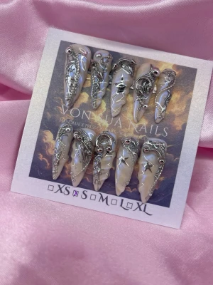 Starbound (S);Long Stiletto - Unika handgjorda press-on naglar i en lång stilettoform. Basen är nude med skimrande pärlemorblå med detaljer i silver, inklusive stjärnor, månar och kedjor. Handgjorda och riktigt statement med 3D-metalldekorationer för en edgy look.S: 15 mm, 11,5 mm, 12 mm, 11 mm, 9 mm .