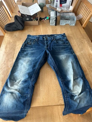 Blå baggy jeans  - Säljer ett par blå baggy jeans med slitna detaljer och ljusa tvättade partier. Jeansen har flera fickor, bred passform och tydliga sömmar. Perfekta för en avslappnad streetwear-look.