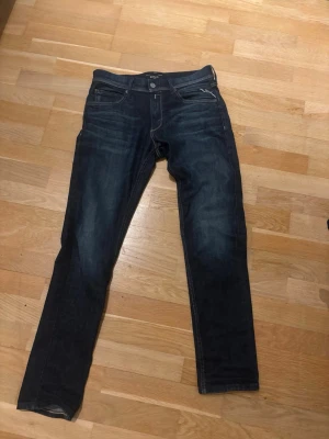 Mörkblå jeans från Replay  - Snygga mörkblå jeans från Replay. Jeansen har diskreta slitningar och kontrastsömmar, samt en läderpatch med logga bak i midjan. Perfekta för en avslappnad och trendig stil. Storlek är 14 år.
