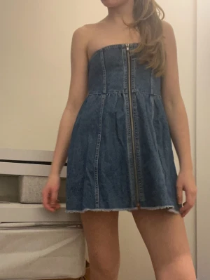 Blå axelbandslös jeansklänning - Axelbandslös kort jeansklänning i blå denim med dragkedja framtill och smock baktill.  Storlek XS, märke okänt det står inte.❤️