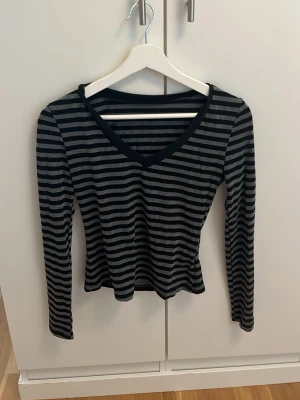 Svart och grå randig långärmad topp - Randig långärmad topp i svart och grått med v-ringning. Tunn och mjuk, perfekt för lager på lager. Snygg passform och klassiskt mönster som funkar till mycket.