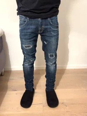 Blå slitna skinny jeans med patchar från Antony morato - Säljer ett par blå skinny jeans med slitningar och patchade detaljer på benen. Jeansen har klassisk femficksmodell, låg midja och är tillverkade i denim med stretch. Snyggt tvättade för en trendig, avslappnad look.