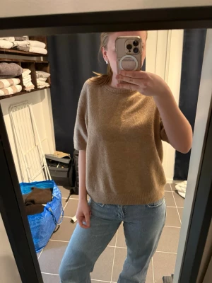Beige stickad tröja från H&M - Stickad tröja från H&M i mjuk beige ton. Tröjan har korta ärmar, rund halsringning och ribbade muddar vid ärmslut och nederkant. Perfekt för lager på lager och enkel att matcha med olika stilar.