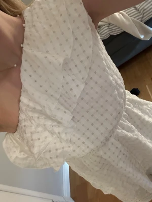 Vit offshoulder blus med volang - Söt vit offshoulder blus med volangdetaljer och diskret rutigt mönster. Blusen har en luftig passform och är tillverkad i ett lätt, strukturerat tyg som känns perfekt för varmare dagar. Perfekt att styla med jeans eller kjol för en trendig look.☺️. vet ej märke då lappen är borta. 