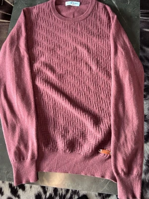 Vinröd stickad tröja Harmont & Blaine - Stickad tröja i vinrött från Harmont & Blaine Jeans. Tröjan har ett snyggt mönster framtill, rund halsringning och ribbade muddar. Materialet känns mjukt och passar perfekt för kyligare dagar.