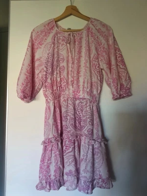  Ny slutsåld Rosa och vit kortklänning med volang - Söt kortklänning i rosa och vitt med blommigt mönster och volangkant. Klänningen har trekvartsärm och resår i midjan för en bekväm passform. Perfekt för sommarens alla tillfällen!