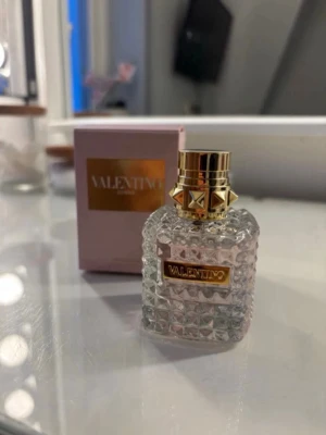 Valentino parfym med nitar och glasflaska - Lyxig parfym från Valentino i en transparent glasflaska med rutmönster och gulddetaljer. Flaskan har en cool guldfärgad kork med nitar och etikett i guld. Kommer med en rosa ask med gulddetaljer. Perfekt för dig som gillar exklusiva dofter. Betalning via vanlig swish! 