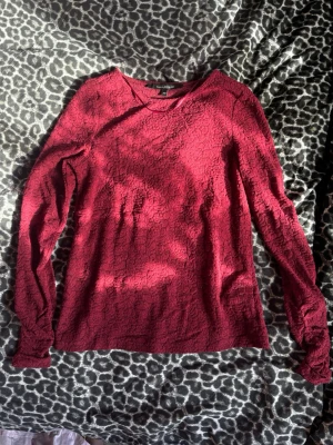 Vinröd långärmad topp med struktur - Säljer en vinröd långärmad topp med snygg struktur och diskret mönster i tyget. Tröjan har rund halsringning och är tillverkad i ett mjukt material som känns bekvämt mot huden. Perfekt för dig som gillar en enkel men ändå unik stil.