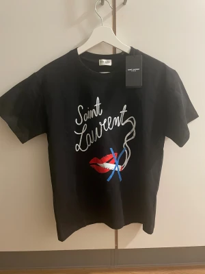 Saint Laurent T-shirt - Svart Saint Laurent T-shirt. Stilren med tryck på framsidan. Oanvänd.