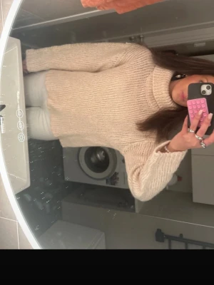 Beige polotröja i grovstickat - Säljer en beige, grovstickad polotröja med avslappnad passform och långa ärmar. Tröjan har bred polokrage och ribbade muddar vid ärmslut och nederkant. Perfekt för att hålla värmen under kyliga dagar.