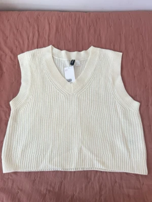 Vit stickad väst från H&M - Snygg vit stickad väst från H&M med bred ribbstickning och v-ringad hals. Perfekt att bära över en skjorta eller t-shirt för en trendig lager-på-lager-look. Klassisk och enkel design som passar till mycket.