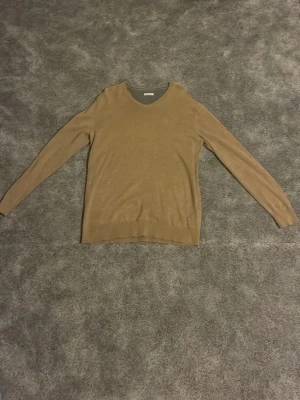 Beige stickad tröja från A.P.C. - Snygg beige stickad tröja från A.P.C. med diskret broderad logga framtill. Tröjan har V-ringning och långa ärmar, perfekt för lager på lager. Tillverkad i mjukt material som känns skönt mot huden.