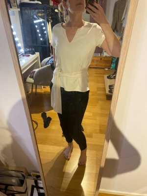 Vit topp med knytband - Stilren vit kvalitetstopp med korta ärmar och knytband i midjan. Lite tjockare tyg som ger en lyxigare känsla. Knytbandet kan man välja att ta bort för att få en rak modell.