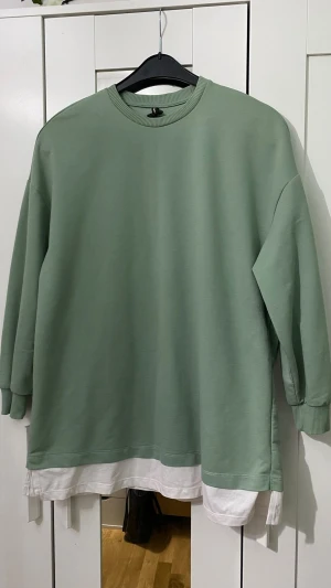 Grön sweatshirt från DeFacto Woman - Oversized ljusgrön sweatshirt från DeFacto Woman med rund halsringning och ribbade muddar. Tröjan har en vit detalj i nederkanten som ger en lager-på-lager-look. Tillverkad i mjukt sweatshirtmaterial, perfekt för en avslappnad stil.