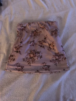 Blommig rosa kjol - Söt kjol i ljusrosa med blommigt mönster i bruna och rosa toner. Kjolen har en rak, enkel passform och är perfekt för varma dagar. Tillverkad i ett mjukt och lätt material som känns skönt mot huden.