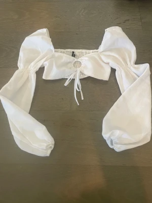 Vit croppad blus med puffärmar - Trendig vit croppad blus från NA-KD med långa puffärmar och knytning framtill. Toppen har en rund cut-out detalj vid bysten och elastisk kant upptill för en snygg passform. Perfekt för dig som vill ha en statement topp till din outfit.