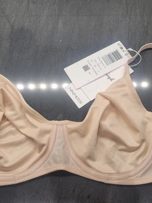 Beige minimizer-bh från Triumph 80 C - Säljer en beige minimizer-bh från Triumph med bygel och släta kupor. Bh:n har justerbara axelband och är tillverkad i ett mjukt, stretchigt material som ger bra stöd och en naturlig siluett. Perfekt för dig som vill ha en diskret och bekväm bh under kläderna. NY med prislapp.