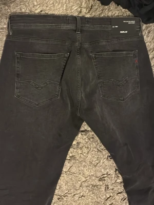 Svarta Replay jeans med raka ben - Säljer ett par svarta jeans från Replay med raka ben och klassisk femficksmodell. Jeansen har diskreta slitningar och tydliga sömmar på bakfickorna. Materialet är mjukt denim som ger en skön passform. Perfekta för dig som gillar en stilren och enkel look. i princip helt nya. Använd en gång passar inte mig jättebra därför jag säljer. 33/34