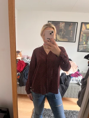 Röd och blå blus - Snygg mörkröd blus med små vita och blå prickar. Blusen har V-ringning och långa ärmar, perfekt till jeans eller kjol. Materialet känns lätt och luftigt, vilket gör den skön att bära hela dagen. 