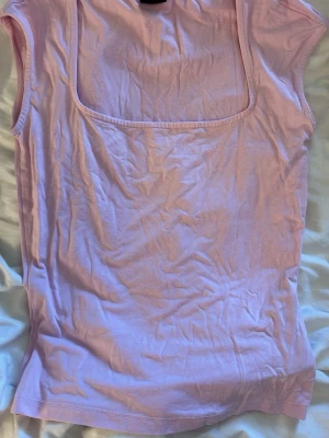 Ljusrosa ärmlös topp Gina Tricot - Säljer en ljusrosa ärmlös topp från Gina Tricot med fyrkantig ringning. Toppen är i mjukt bomullsmaterial och har en enkel, clean design som passar perfekt till jeans eller kjol.