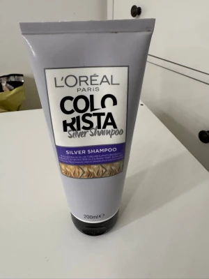 L'Oréal Colorista Silver Shampoo - Lila tub med L'Oréal Paris Colorista Silver Shampoo, 200 ml. Speciellt framtaget för att neutralisera gula toner i blont eller blekt hår. Tuben har svart lock och modern design med tydlig text och illustration av blont hår. Testad ca 4ggr. 