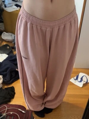 Iets Frans Harri Joggers - Säljer ett par ljusrosa mjukisbyxor från Iets Frans med avslappnad passform och resår i midjan. Byxorna har en broderad logga på sidan och är gjorda i mjukt bomullsmaterial. Byxorna har en dragsko så man kan justera längden! Perfekta för chill dagar hemma eller när du vill vara extra bekväm. De är storlek M och oversize (jag är 158cm för referens).