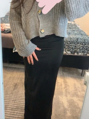 Svart långkjol med slits - Säljer en svart långkjol med slits på sidan. Kjolen har en tight passform och är gjord i ett mjukt, stretchigt material som ger en snygg siluett. 