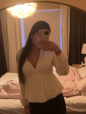 Vit/beige blus med v-ringad - Säljer en vit/beige v-ringning och långärmad design. Blusen har en lätt strukturerad yta och volang nedtill som ger en feminin siluett. Knappt använd.