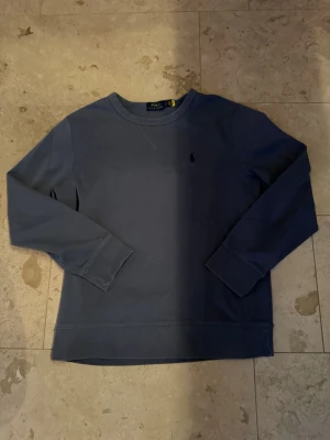 Blå sweatshirt Polo Ralph Lauren - Ljusblå sweatshirt från Polo Ralph Lauren med rund halsringning och diskret broderad logga på bröstet. Tröjan har långa ärmar och breda muddar vid ärmslut och nederkant. Tillverkad i mjuk bomull för en skön känsla.