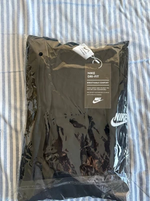 Svart Nike Dri-Fit t-shirt - Snygg svart t-shirt från Nike med klassisk vit logga på bröstet. Tillverkad i Dri-Fit material som andas och håller dig bekväm hela dagen. Perfekt för dig som gillar sportig och enkel stil.