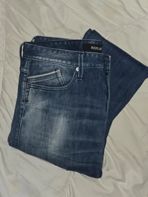 Blå Replay jeans herr w32 L32 - Säljer ett par blå jeans från Replay med snygga slitningar och tvättad look. Klassisk femficksmodell med dragkedja och knapp. Jeansen har raka ben och är tillverkade i bomull med en skön stretch. Perfekta för en avslappnad och trendig stil.
