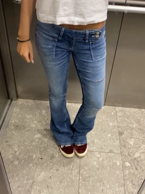 Blå bootcut jeans  - Snygga blå bootcut jeans med dubbla knappar i midjan och slitningar vid knäna. Använda men dom är i väldigt bra skick!