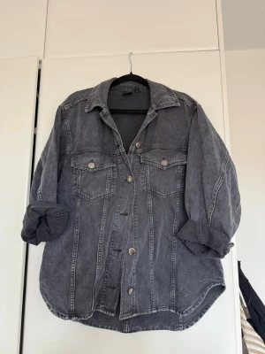 Oversized svartgrå jeansjacka - Snygg oversized jeansjacka från H&M i svartgrå tvätt. Klassisk modell med två bröstfickor med lock och knappar, samt knappstängning framtill. Jackan har nedhasade axlar och uppvikta ärmar för en avslappnad look. Perfekt till streetwear-stilen.