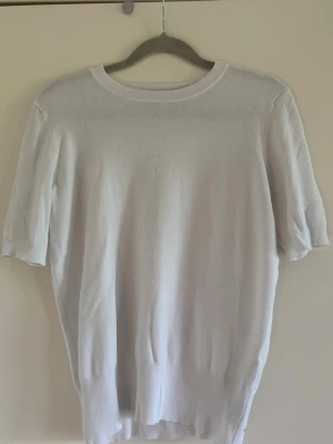 Vit stickad kortärmad topp - En enkel och stilren vit stickad topp med rund halsringning och korta ärmar. Materialet är mjukt och stretchigt, vilket ger en bekväm passform. Perfekt att matcha med jeans eller kjol för en clean look.