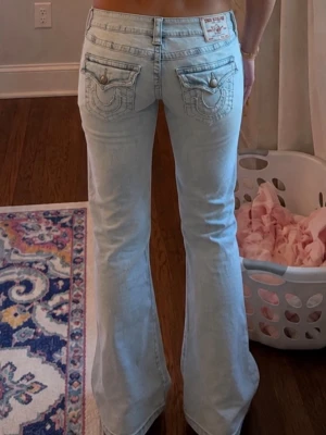 Ljusblå bootcut jeans True Religion - Säljer ett par ljusblå bootcut jeans från True Religion med ikoniska broderade fickor bak och låg midja. Jeansen har klassisk femficksdesign och är tillverkade i denim med en lätt tvättad look. Perfekta för dig som gillar retrovibbar och snygga detaljer.