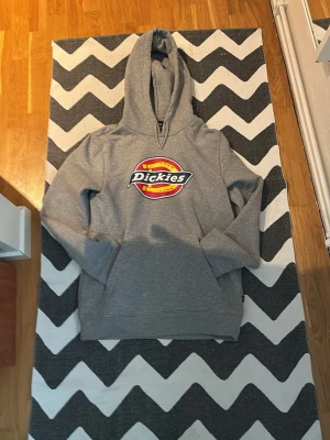 Grå Dickies hoodie med logga - Tjena! Säljer min gråa hoodie från Dickies med stor färgglad logga på bröstet. Klassisk modell med huva och känguruficka framtill. Tillverkad i mjukt sweatshirtmaterial som är perfekt för chill dagar. Passar dig som gillar streetwear och enkel stil. Passar om man är ca160-170 MVH Strwwt Wst