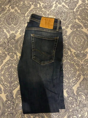 Mörkblå jeans från Jack & Jones  slim fit - Snygga mörkblå jeans från Jack & Jones med klassisk femficksdesign och kontrastsömmar. Jeansen har en rak passform och är tillverkade i denim med en lätt tvättad look. Perfekta för en avslappnad och trendig stil.