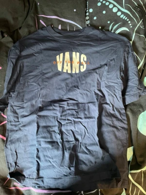 Svart Vans t-shirt baggy fit - Snygg svart t-shirt från Vans med baggy fit och stort tryck 'VANS OFF THE WALL' på bröstet. Tillverkad i 100% bomull för en skön och avslappnad känsla. Perfekt för dig som gillar streetwear och vill ha en enkel men stilren look.