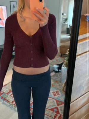 Vinröd ribbad kofta från Kappahl - Snygg vinröd ribbad kofta från Kappahl med v-ringning och knappar framtill. Kortare modell med långa ärmar, perfekt att styla till både jeans och kjol. Tillverkad i mjukt, stretchigt material som sitter tajt och bekvämt.