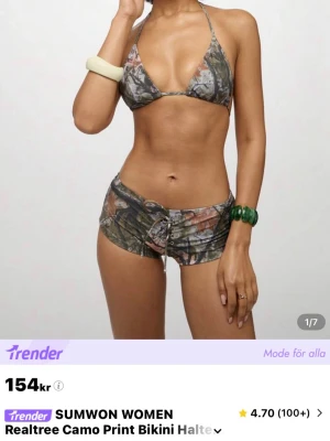 Camo bikini med snörning från Sumwon - Trendigt bikini-set från Sumwon med camouflagemönster i gröna och bruna toner. Överdelen är trekantsmodell med halterneck och underdelen är shorts med snörningsdetalj framtill. Perfekt för sommaren och strandhäng.