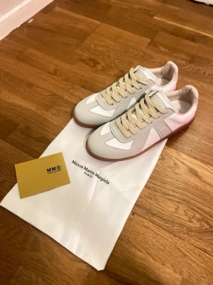 Maison Margiela sneakers vita/grå - Maison Margiela sneakers i vitt och ljusgrått läder och mocka med beigea skosnören och klassisk gummisula. Snygg och stilren siluett som passar till många outfits. Kommer med dustbag och originalkort.