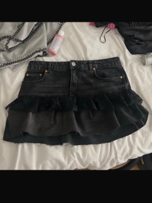 Svart jeanskjol med volang - Cool svart jeanskjol från Levi's med volangdetaljer och rå kant. Kjolen har klassiska fickor fram och bak, knapp och dragkedja. Perfekt för dig som gillar en edgy och trendig look.
