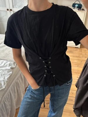 T-shirt med snörning  - Så cool T-shirt med snörning! En av öglorna har lossnat, men inget man tänker på💕storlek L, men skulle säga mer som M